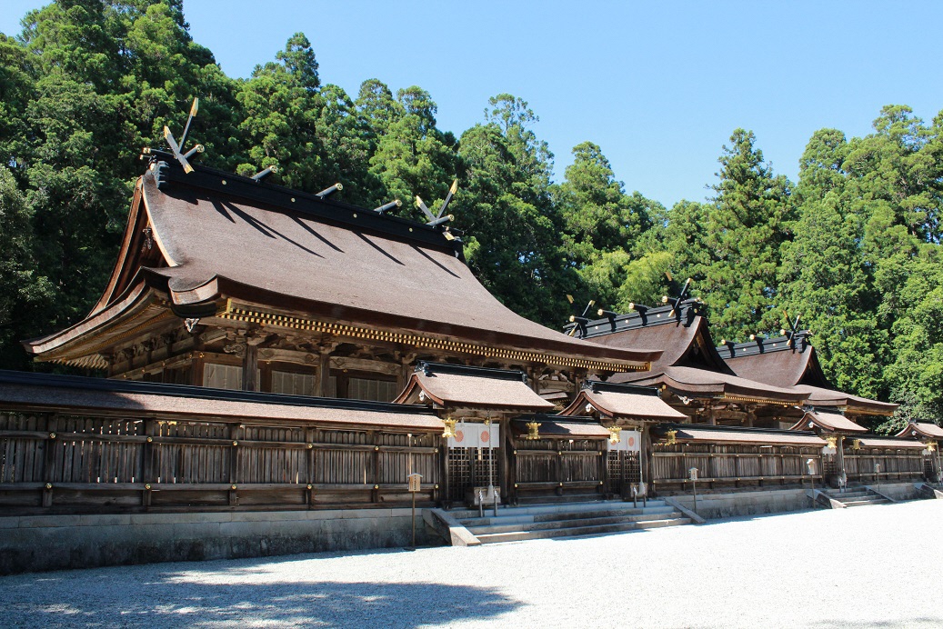 The shrine buildings of Kumano Hongu Taisha beneath blue sky and trees