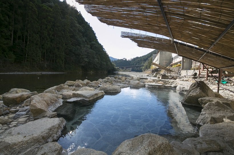 A rock-lined outdoor hot spring bath beside a river